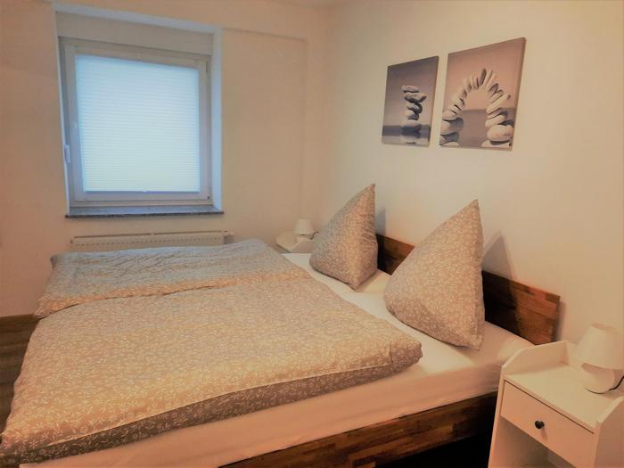 Foto aus dem Schlafzimmer. Holzbett und graue Bettwäsche mit grauen Leinwandbildern an der Wand des Kopfbettes