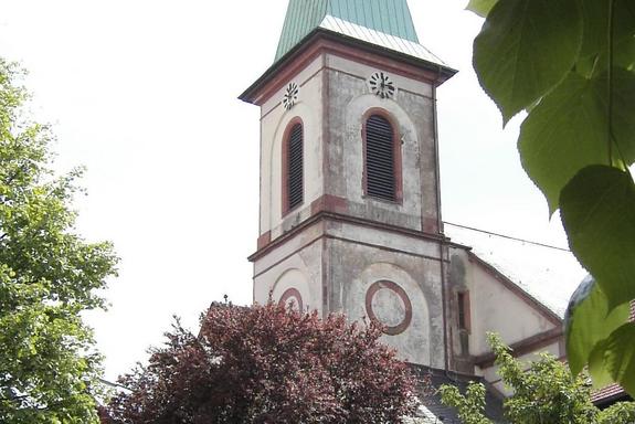 Eine Pfarrkirche mit hellgrünem Dach und Bäumen rundherum.