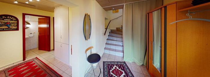 Foto vom Flur mit rotem Teppich, einer Holzgarderobe und einer Treppe, die nach oben führt