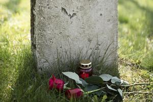Grabstein mit mit zwei roten Rosen und einer roten Kerze