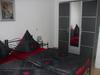 Bild vom Schlafzimmer: Grauer Metallbett mit roter/grauer Bettwäsche und einem grauen Spielgelkleiderschrank