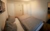 Foto aus dem Schlafzimmer. Graue Bettwäsche mit weißer Zimmertür und weißem Kleiderschrank