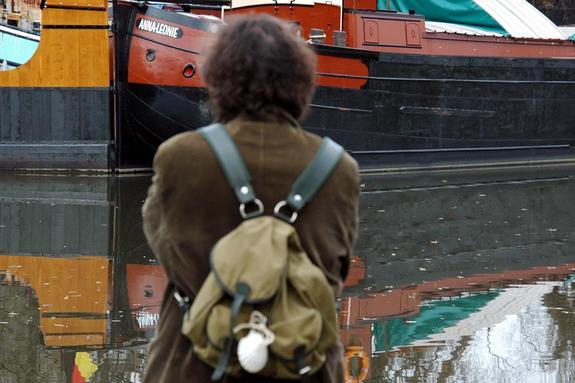 Ein Mann von hinten mit einem Rucksack, der eine Wand betrachtet. Diese Wand ist ein Stück eines Schiffes