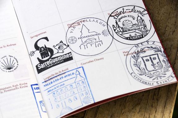 Pilgerpass liegt aufgeschlagen auf dem Tisch. Auf der aufgeschlagenen Seite sieht man 5 verschiedene Pilger-Stempelabdrücke