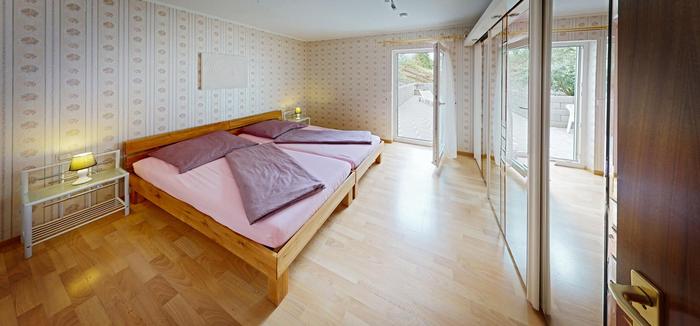 Foto vom Schlafzimmer. Heller Eichenboden mit rosa Bettwäsche und Spiegelholzkleiderschrank an der rechten Wandseite
