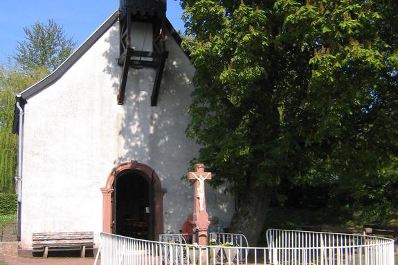 Eine kleine weiße Kapelle. rechts neben der Kapelle befindet sich ein großer grüner Baum