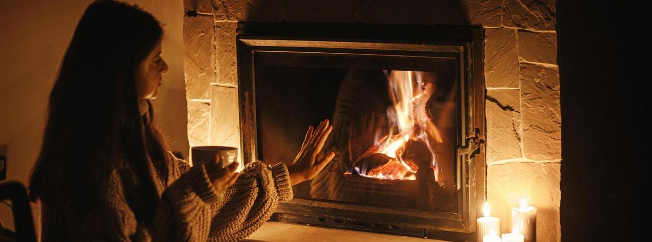 Woman hands holding cup of tea and warming up at cozy fireplace 