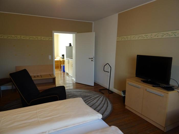 Helles Schlafzimmer mit hellgelben Wänden. Einem Fernseher und TV-Board an der Wand.