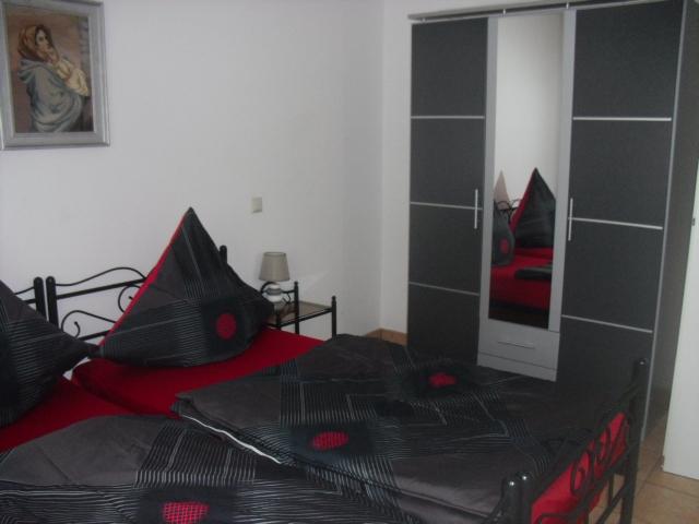 Bild vom Schlafzimmer: Grauer Metallbett mit roter/grauer Bettwäsche und einem grauen Spielgelkleiderschrank